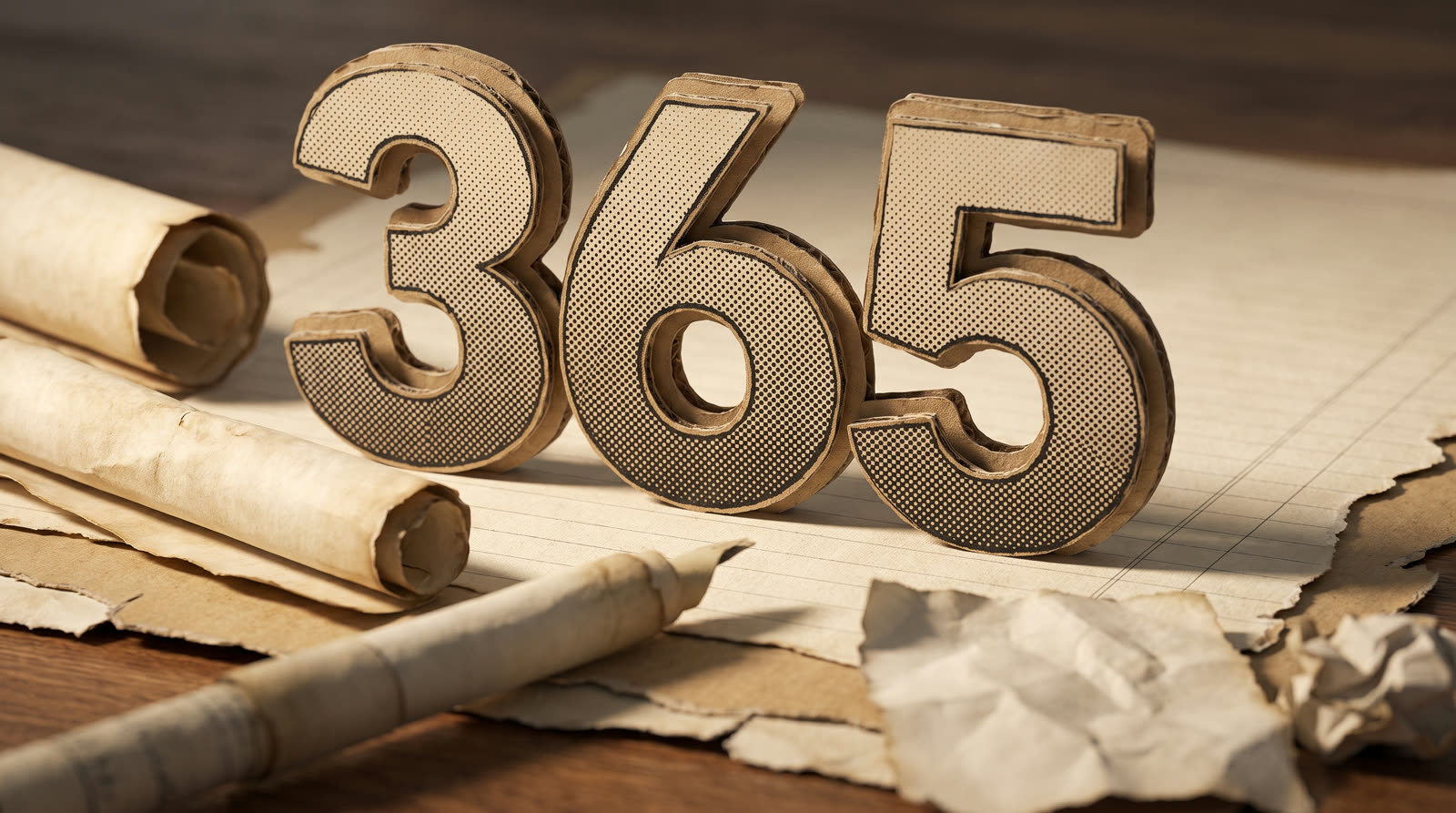 A cardboard numeral 365 standing on a lined page beside rolled scrolls and a quill, warm desk light.